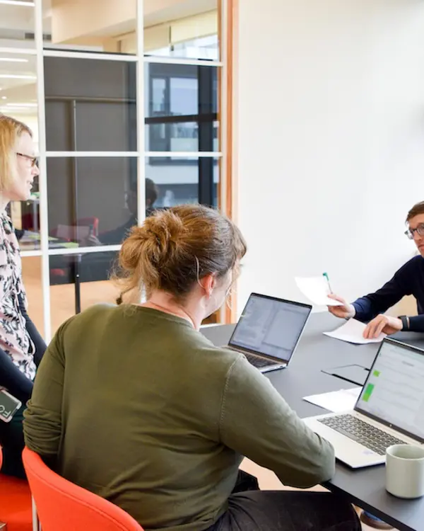 Two Programme Directors, Gemma and Sarah, looking at concept papers with their Technical Specialist, Dan. They have pieces of paper spread over a table and are talking. 