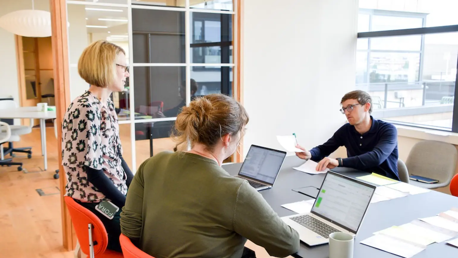 Two Programme Directors, Gemma and Sarah, looking at concept papers with their Technical Specialist, Dan. They have pieces of paper spread over a table and are talking. 