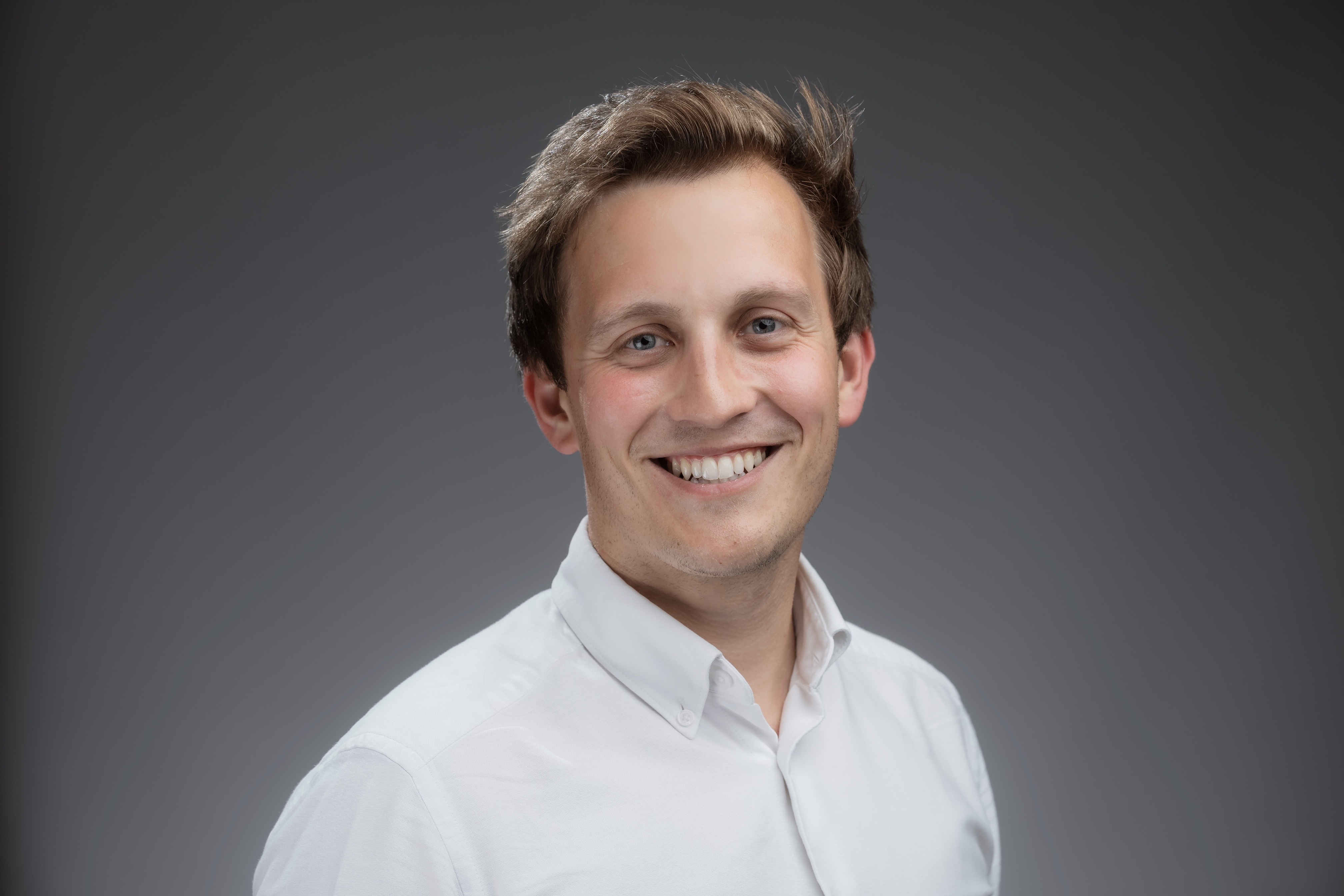 A photo of David Stringer smiling in front of a grey wall.