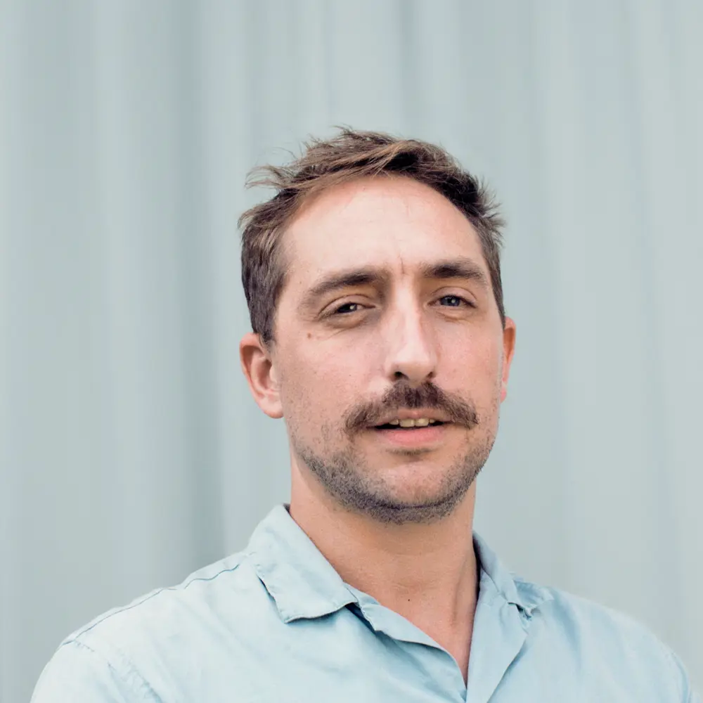 A photo of Jacques looking at the camera, he is sat against a blue background.